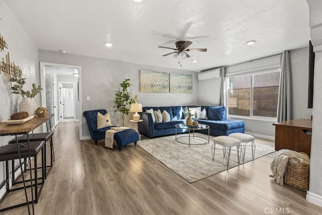 living room featuring wood-type flooring, an AC wall unit, a textured ceiling, and ceiling fan