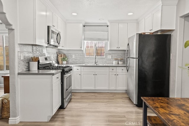 kitchen with sink, tasteful backsplash, light wood-type flooring, stainless steel appliances, and white cabinets