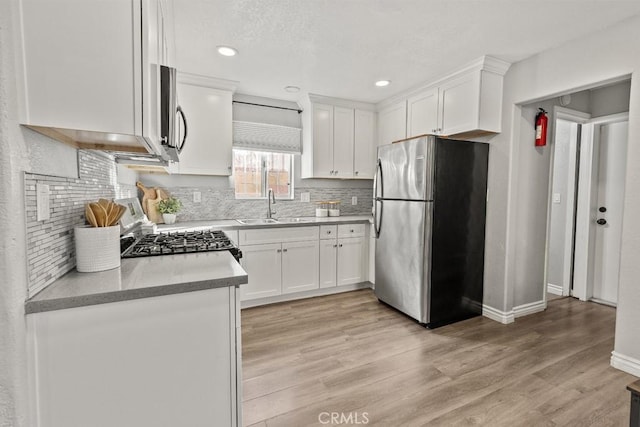 kitchen with stainless steel refrigerator, white cabinetry, sink, range, and light hardwood / wood-style flooring