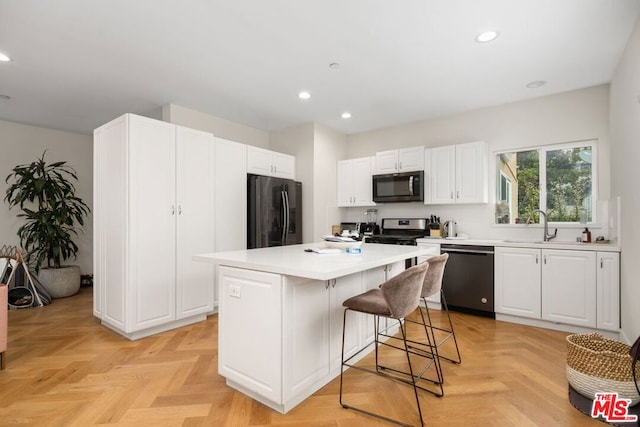 kitchen featuring stainless steel appliances, a breakfast bar, a kitchen island, light parquet flooring, and white cabinets