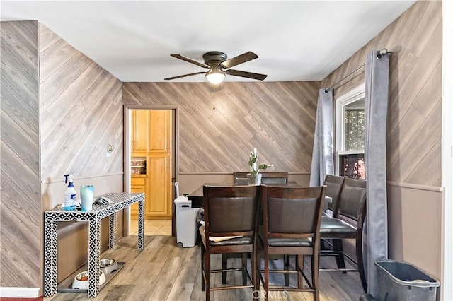 dining space with wooden walls, ceiling fan, and light hardwood / wood-style floors