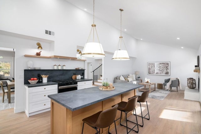 kitchen with a kitchen bar, white cabinetry, light wood-type flooring, black range with gas stovetop, and pendant lighting