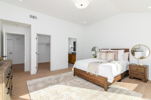 bedroom with ensuite bath, a spacious closet, light hardwood / wood-style floors, and vaulted ceiling