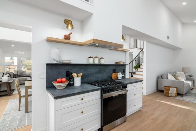 kitchen with a high ceiling, gas stove, light hardwood / wood-style flooring, and white cabinets