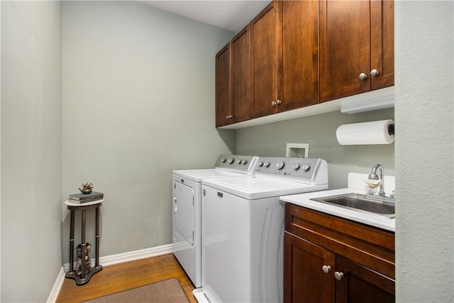 clothes washing area with cabinets, sink, washing machine and clothes dryer, and light hardwood / wood-style flooring