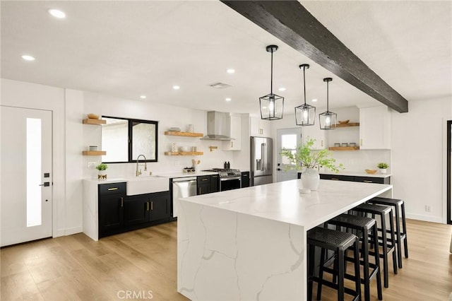 kitchen with a large island, appliances with stainless steel finishes, hanging light fixtures, light stone countertops, and wall chimney exhaust hood