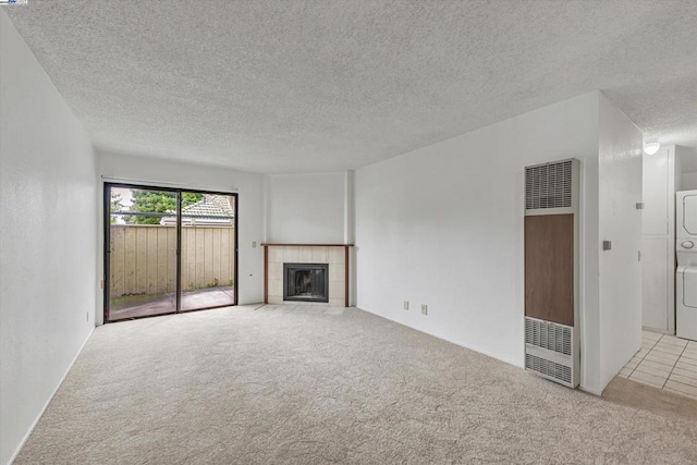 unfurnished living room featuring stacked washer / dryer, light colored carpet, a textured ceiling, and a fireplace