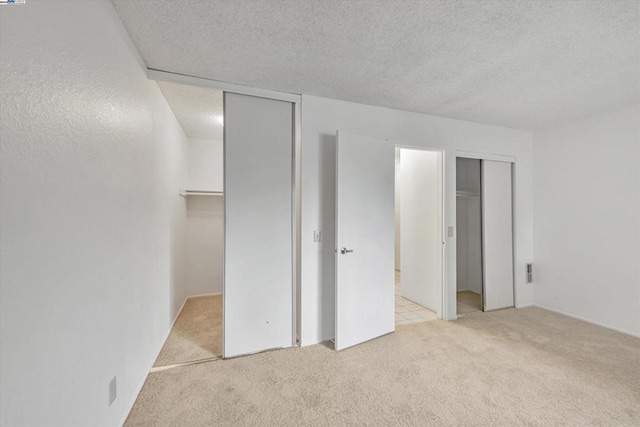 unfurnished bedroom with two closets, light colored carpet, and a textured ceiling