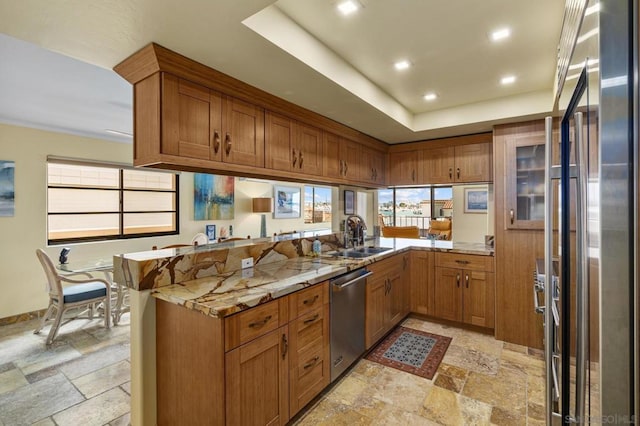 kitchen with a raised ceiling, sink, light stone counters, kitchen peninsula, and stainless steel appliances