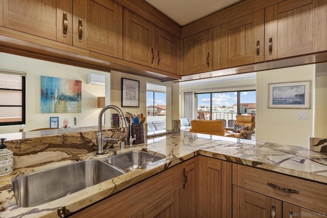 kitchen with sink, a wall unit AC, light stone counters, and kitchen peninsula