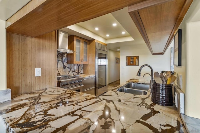 kitchen featuring wall chimney exhaust hood, sink, high end appliances, tasteful backsplash, and kitchen peninsula