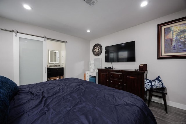 bedroom with a barn door, dark hardwood / wood-style floors, and connected bathroom