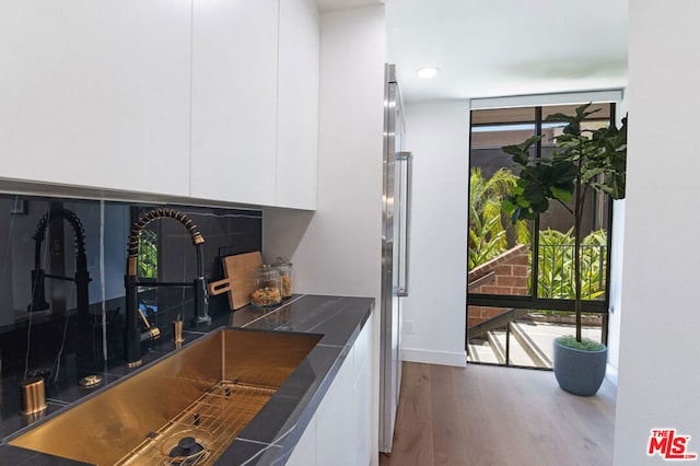 kitchen with white cabinetry, expansive windows, sink, and hardwood / wood-style flooring