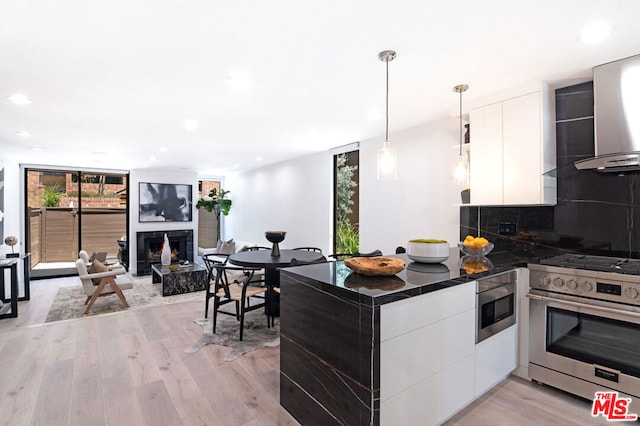 kitchen with appliances with stainless steel finishes, white cabinets, pendant lighting, light hardwood / wood-style floors, and backsplash