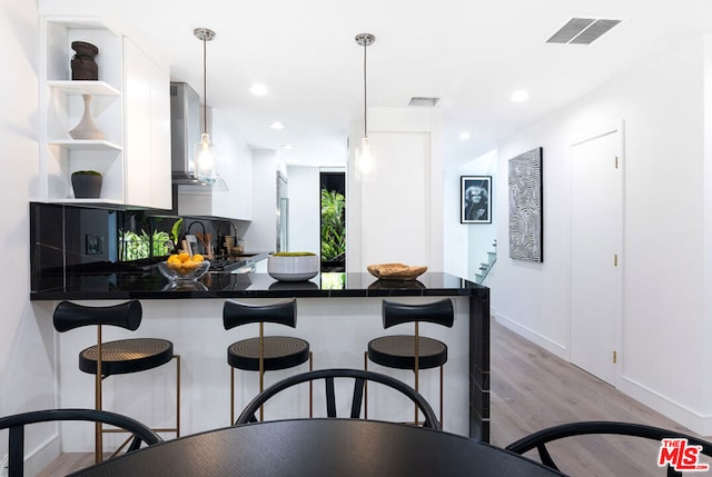 kitchen featuring white cabinetry, wall chimney range hood, decorative light fixtures, and kitchen peninsula