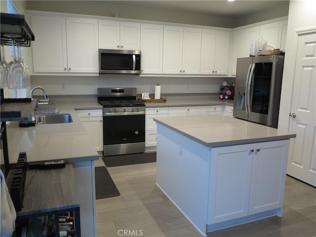 kitchen with a kitchen island, appliances with stainless steel finishes, sink, white cabinets, and light hardwood / wood-style floors