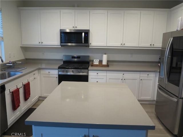 kitchen with sink, hardwood / wood-style flooring, appliances with stainless steel finishes, white cabinetry, and a center island