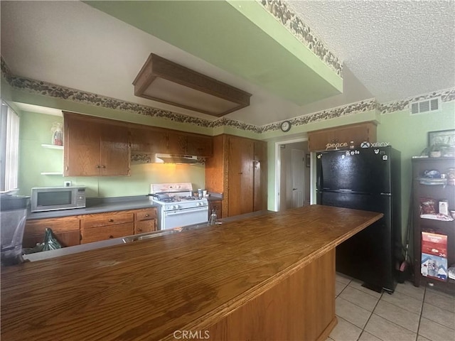 kitchen with white range with gas cooktop, light tile patterned floors, a textured ceiling, and black fridge