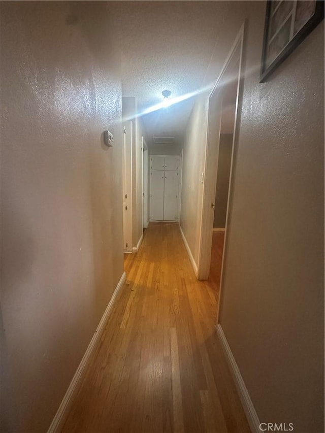 hall with light hardwood / wood-style floors and a textured ceiling