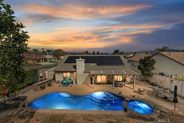 pool at dusk featuring a patio area and an in ground hot tub