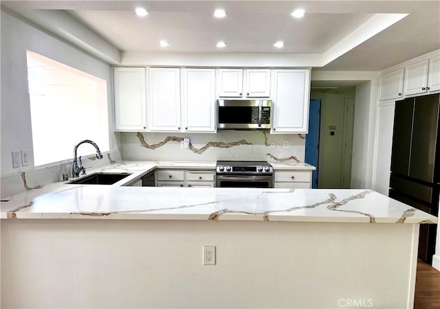 kitchen with kitchen peninsula, stainless steel appliances, sink, light stone counters, and white cabinets