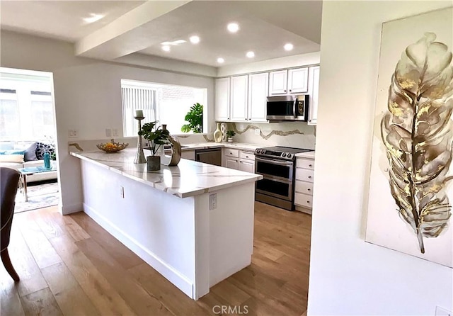 kitchen with light stone counters, recessed lighting, stainless steel appliances, a peninsula, and light wood-style floors