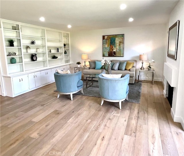 living area with baseboards, light wood-type flooring, a fireplace, and recessed lighting