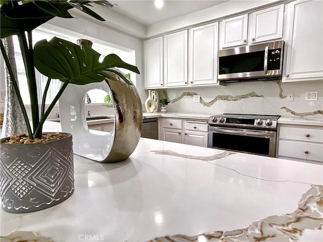 kitchen featuring appliances with stainless steel finishes, decorative backsplash, light stone countertops, and white cabinets