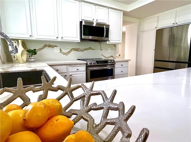 kitchen with light stone countertops, white cabinetry, stainless steel appliances, and a sink