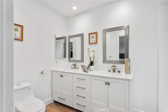 full bath featuring double vanity, a sink, toilet, and wood finished floors