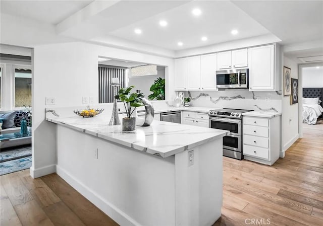kitchen with stainless steel appliances, light wood-style floors, a peninsula, and light stone countertops