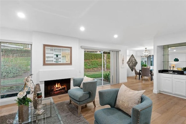 sitting room featuring recessed lighting, baseboards, light wood-style floors, a lit fireplace, and an inviting chandelier