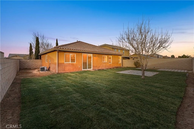 back house at dusk featuring central AC, a patio area, and a lawn