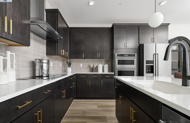 kitchen featuring wall chimney exhaust hood, sink, decorative light fixtures, appliances with stainless steel finishes, and backsplash