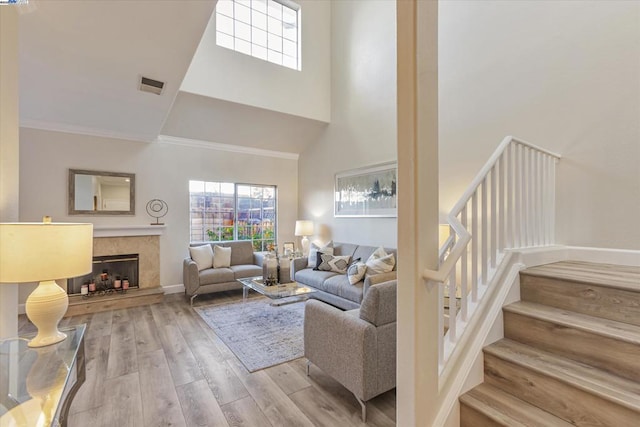 living room with a towering ceiling, ornamental molding, a premium fireplace, and light wood-type flooring