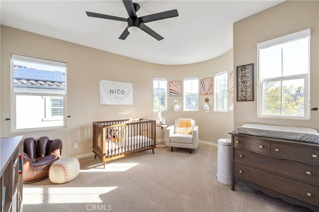 bedroom featuring light carpet, a nursery area, and ceiling fan