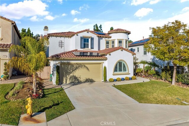 mediterranean / spanish house featuring a garage, solar panels, and a front lawn