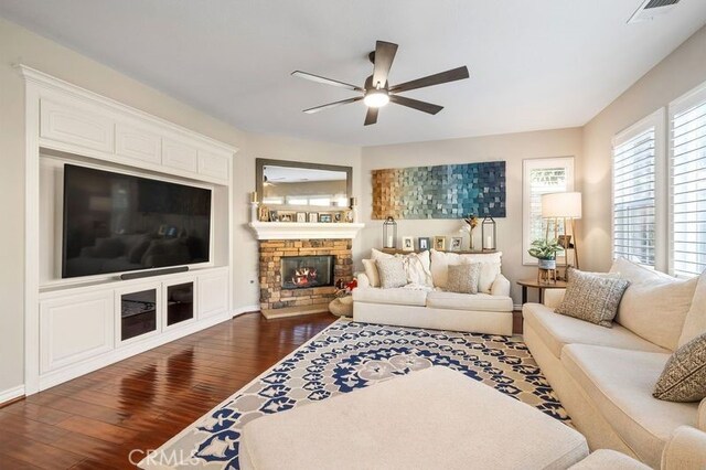 living room with dark wood-type flooring, ceiling fan, and a stone fireplace