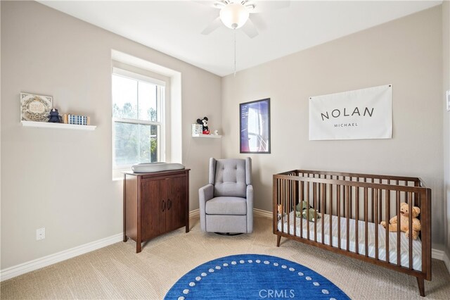 bedroom featuring a nursery area, carpet flooring, and ceiling fan