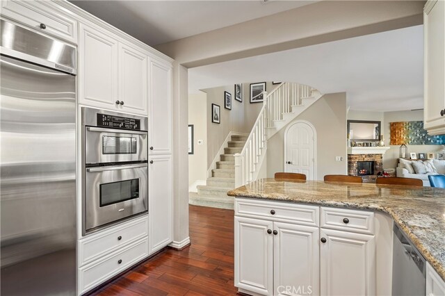 kitchen with a stone fireplace, dark hardwood / wood-style floors, white cabinetry, light stone counters, and stainless steel appliances