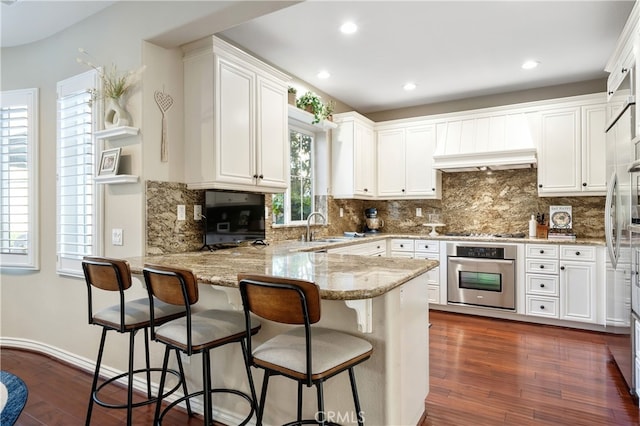 kitchen featuring white cabinetry, dark hardwood / wood-style floors, light stone counters, kitchen peninsula, and oven