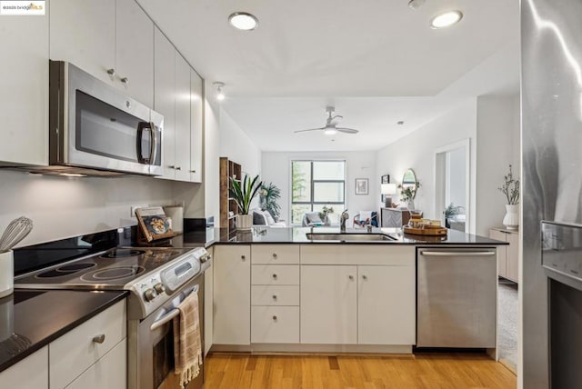 kitchen with sink, appliances with stainless steel finishes, kitchen peninsula, ceiling fan, and light hardwood / wood-style floors