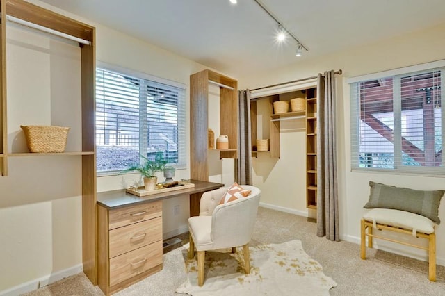 living area featuring rail lighting, built in desk, and light colored carpet