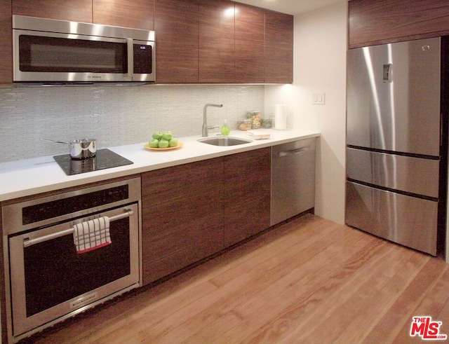 kitchen with sink, backsplash, light hardwood / wood-style floors, dark brown cabinetry, and stainless steel appliances