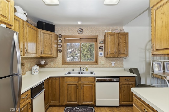 kitchen featuring freestanding refrigerator, light countertops, white dishwasher, and a sink