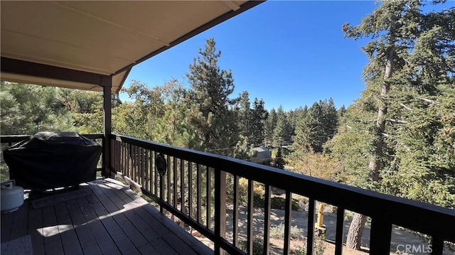 wooden deck featuring a forest view and a grill