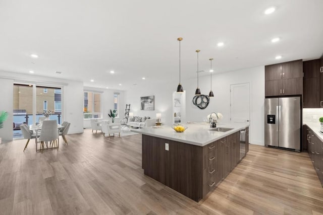 kitchen with sink, a center island with sink, light wood-type flooring, appliances with stainless steel finishes, and pendant lighting