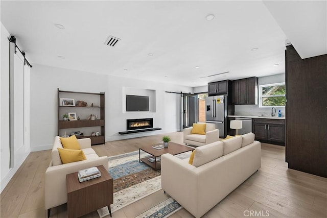 living room with a barn door, visible vents, light wood-style flooring, and recessed lighting