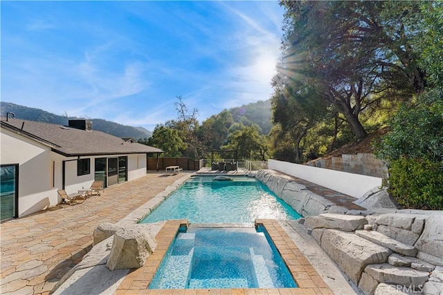 view of swimming pool featuring a pool with connected hot tub, a fenced backyard, and a mountain view