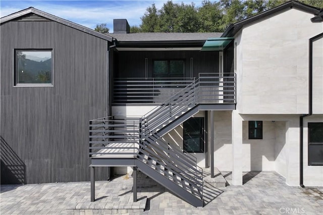 rear view of property featuring a chimney, a patio area, and stairway